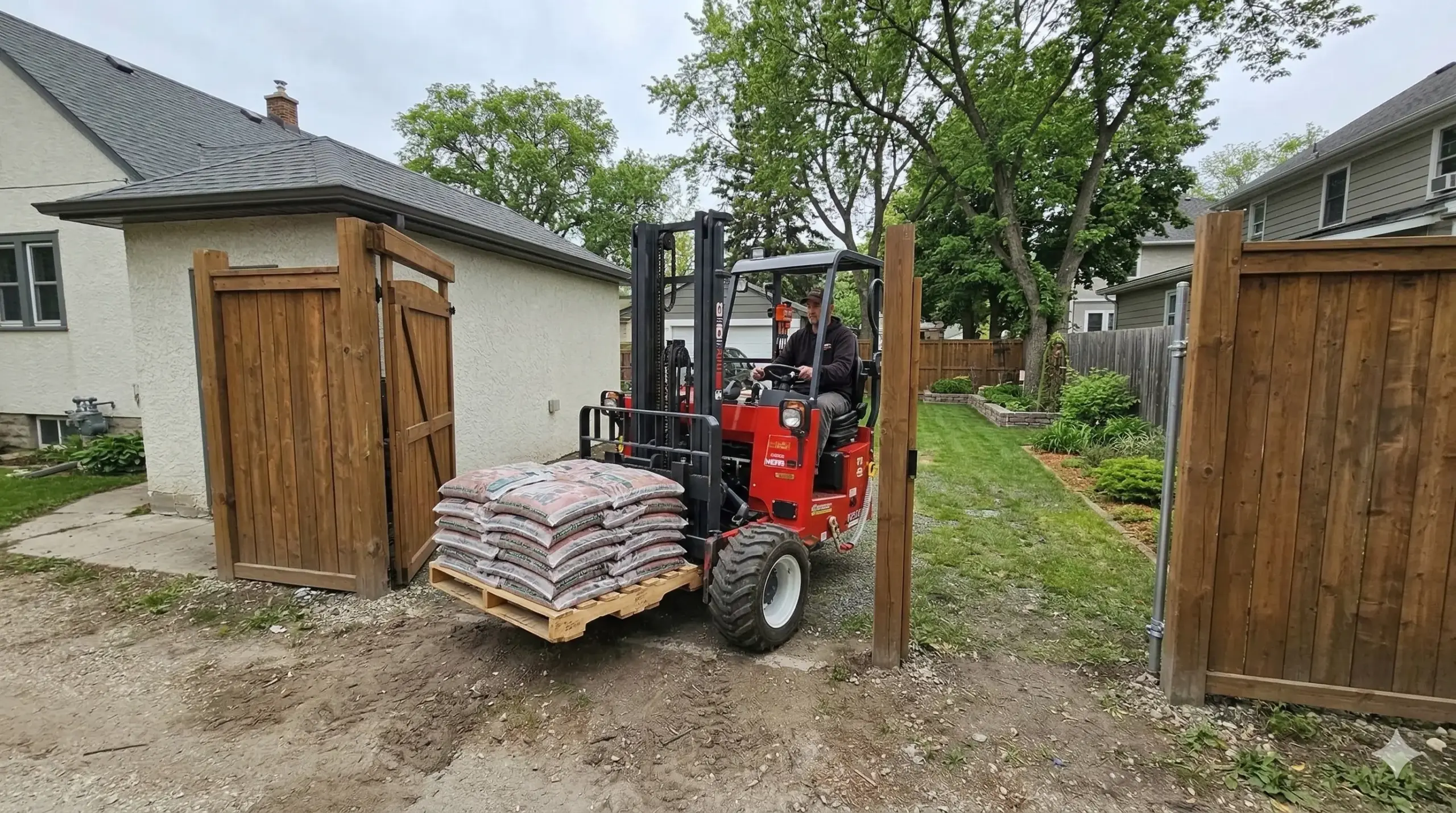 Moffett forklift navigating through narrow residential side gate in Winnipeg to deliver landscaping materials to backyard